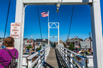 Rear view of woman on footbridge against blue sky