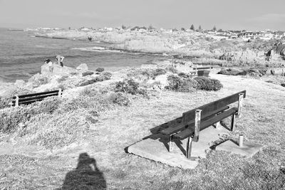 High angle view of empty bench on field by sea against sky