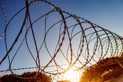 Low angle view of barbed wire against sky during sunset