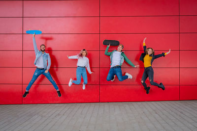 Full length of people jumping against red wall