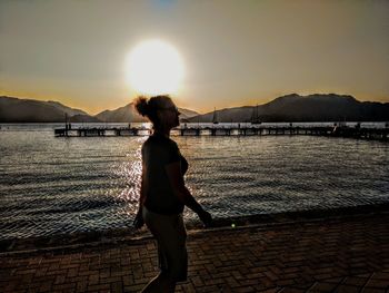 Woman standing on beach against sky during sunset