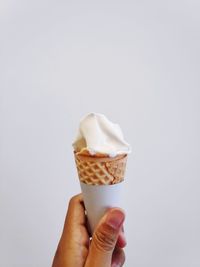 Close-up of hand holding ice cream cone against white background