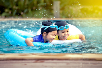 Happy sisters with inflatable rings swimming in pool