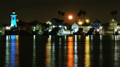 Illuminated buildings by sea against sky at night