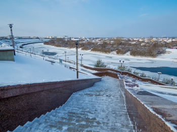 Snow covered road by city against sky