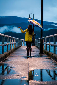 Rear view of woman with umbrella walking on pier over lake against mountains