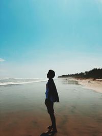 Side view of man standing on beach against sky