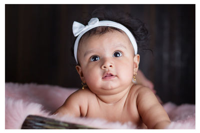 Shirtless cute baby girl looking up while lying on bed at home