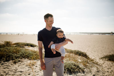 Father smiling & casually holding son on beach