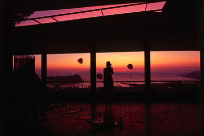 Silhouette man standing by sea against orange sky