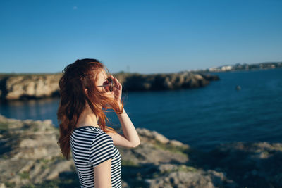 Young woman wearing sunglasses standing by sea against sky