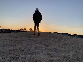 Rear view of man standing on field against sky during sunset