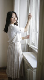 Portrait of young woman opening window at home