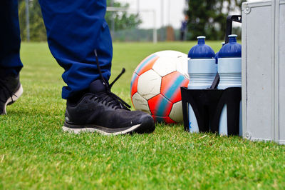 Low section of man walking by ball and bottles on soccer field