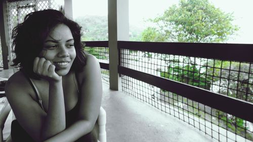 Smiling woman looking away while sitting on chair at balcony