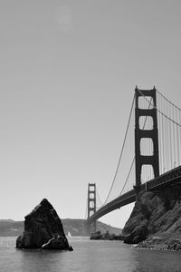 Rock in sea by golden gate bridge against clear sky