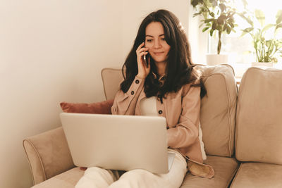 A young female freelancer works online using a phone and laptop at home. online training