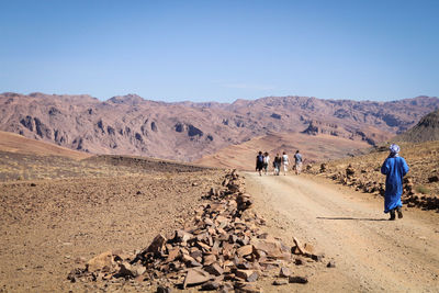 People walking on pathway leading towards mountain against sky