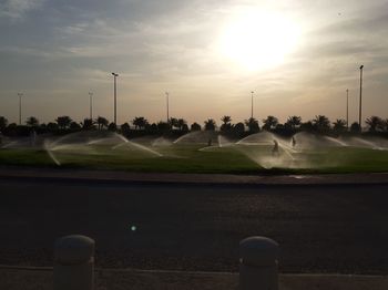 Street by field against sky during sunset