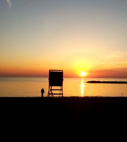 Silhouette chair on beach against sky during sunset