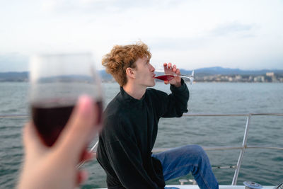 Side view of young man photographing sea against sky