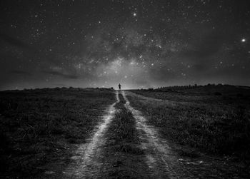 Dirt road on field against sky at night