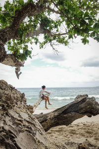 Man standing on rock by sea against sky