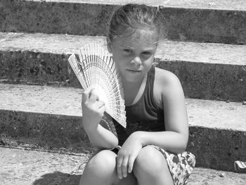 Portrait of girl holding hand fan while sitting on staircase