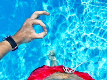 Low section of man showing ok sign while standing in swimming pool