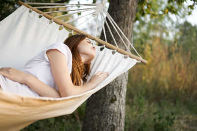 Young woman sitting on hammock against trees