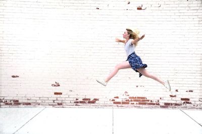 Full length of woman levitating on sidewalk against brick wall