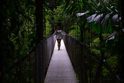 Rear view of woman walking on footbridge in forest