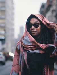 Portrait of young woman standing against wall in city