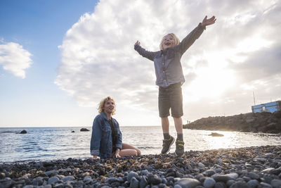 Smiling mother looking at playful son while sitting against sea