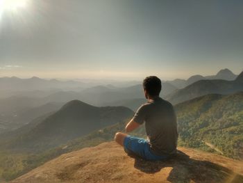 Rear view of man sitting on mountain against sky