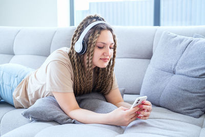 Hipster woman using smart phone lying on sofa