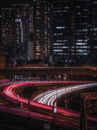 Light trails on road against illuminated buildings at night