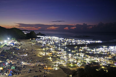 High angle view of illuminated city by sea at night