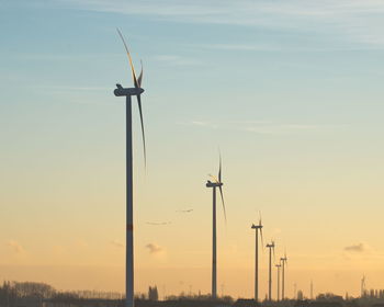 Low angle view of wind turbine against sky during sunset