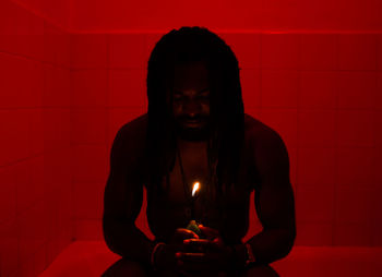 Man holding burning candle while sitting in bathroom