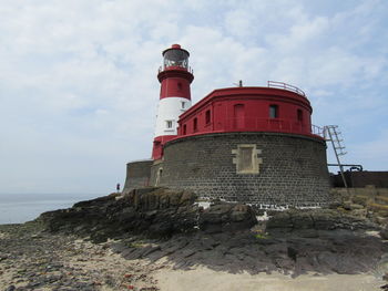 Low angle view of lighthouse by building against sky