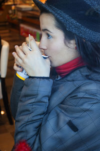 Side view of woman wearing warm clothing while drinking coffee in cafe