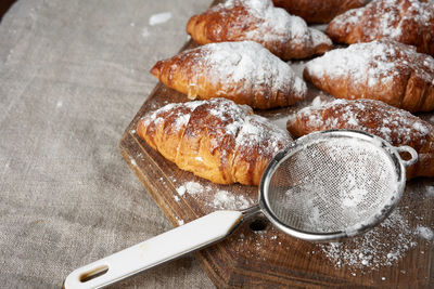 Baked croissants sprinkled with powdered sugar lie on a brown wooden board, close up