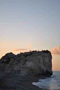 Rock formation on beach against sky during sunset