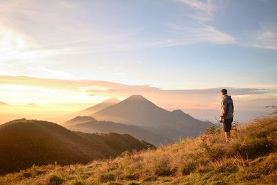 Rear view of man standing on mountain against sunset sky