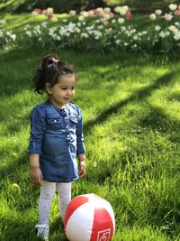 Cute girl standing by ball on field