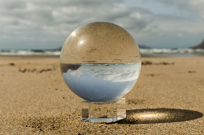 Close-up of crystal ball on beach against sky