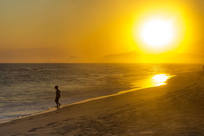 Silhouette man standing on beach against sky during sunset