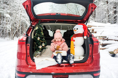 Cute girl with christmas decoration sitting in car trunk during winter