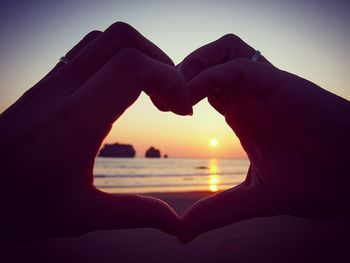Cropped image of woman making heart shape with hands at beach against sky